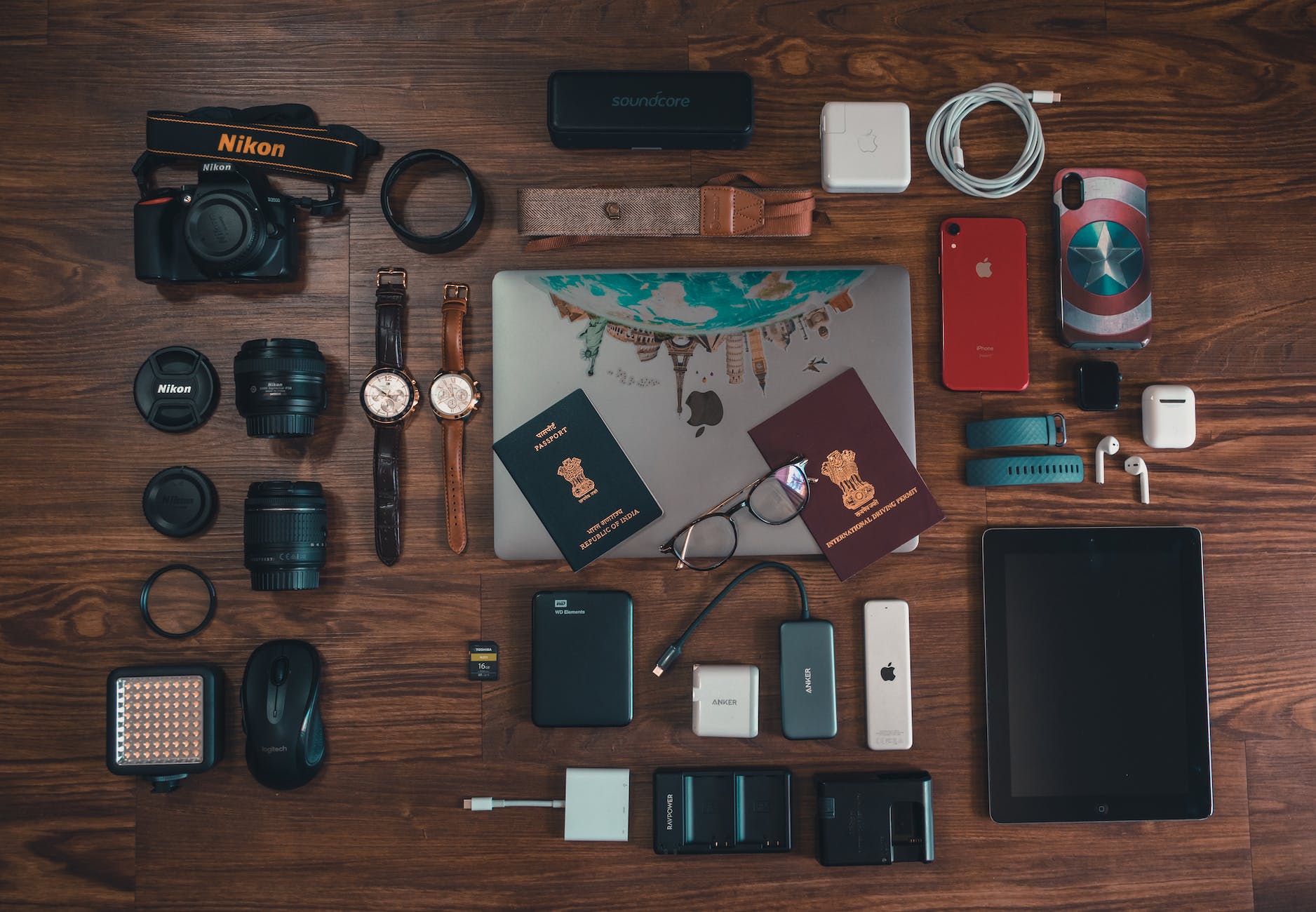 passports camera battery charger watches and cables on brown wooden surface